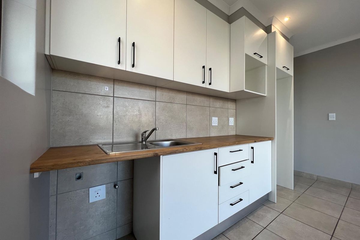 Modern kitchen featuring white cabinetry, wood-look countertops, tiled backsplash, and a stainless steel sink with integrated plumbing connections.