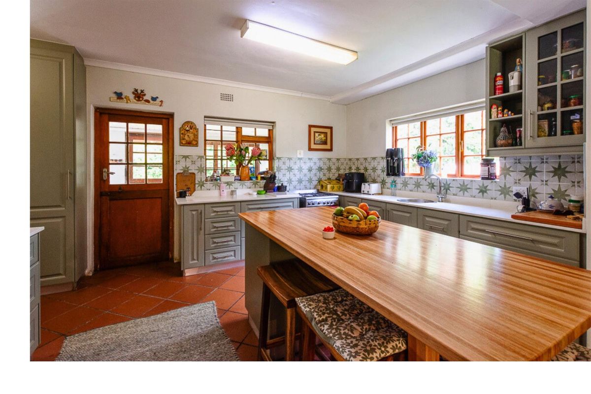 A farmhouse-style kitchen featuring sage green cabinetry, a wooden island countertop, tiled backsplash, and terracotta floor tiles with direct exterior access.