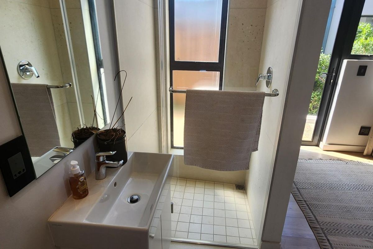 Modern bathroom featuring a sleek vanity basin, wall-mounted mirror, and a tiled shower enclosure with direct access to an outdoor area.