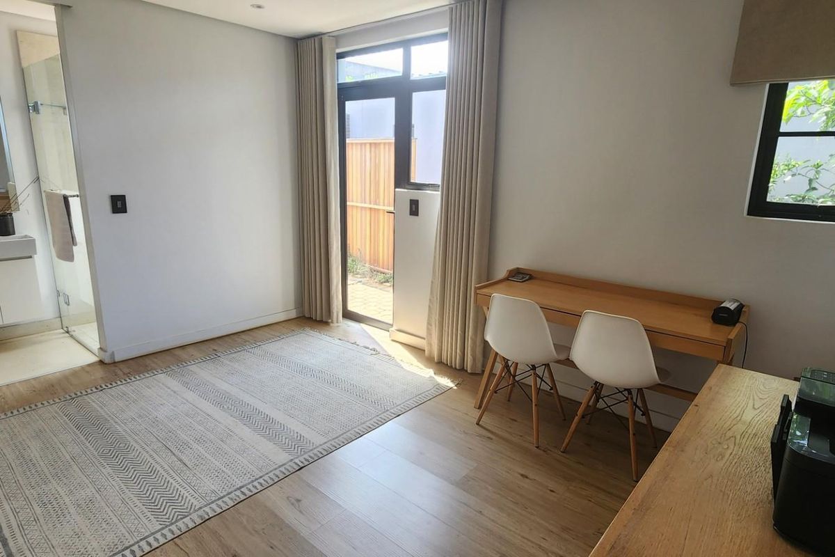 A bright bedroom featuring light wood flooring, an en-suite bathroom with a glass shower, and direct access to an outdoor area via a glass door.