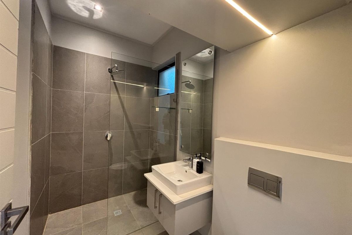 Modern bathroom featuring a walk-in glass shower, wall-mounted vanity with basin, and contemporary tiled finishes with integrated lighting.