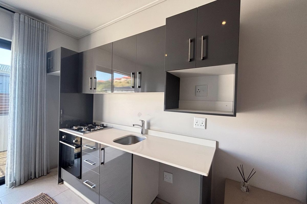 Modern compact kitchen featuring high-gloss grey cabinetry, stone-look countertops, a built-in oven, gas hob, and an integrated sink with a sleek mixer tap.