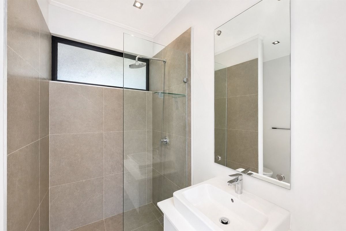 Modern bathroom featuring a walk-in shower with glass screen, contemporary vanity basin, large wall mirror, and neutral ceramic tiling.