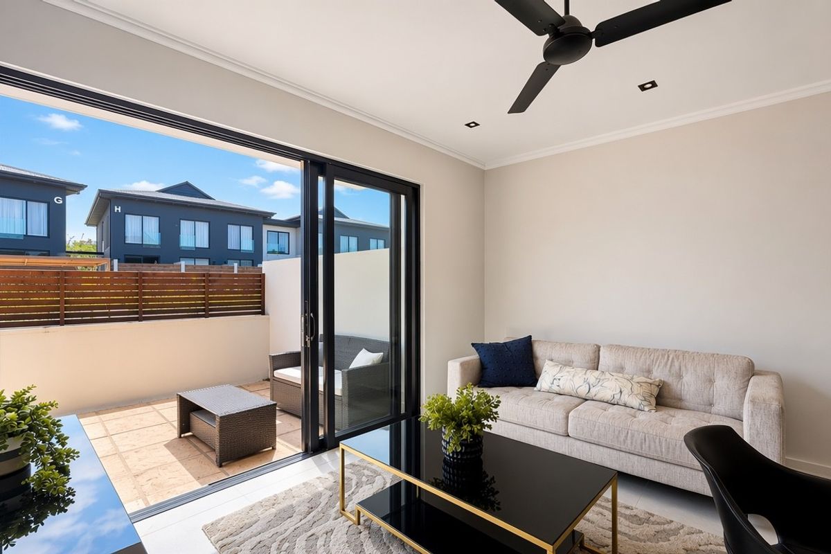 Modern living room featuring large sliding glass doors that open onto a private patio, complemented by a ceiling fan and neutral finishes.