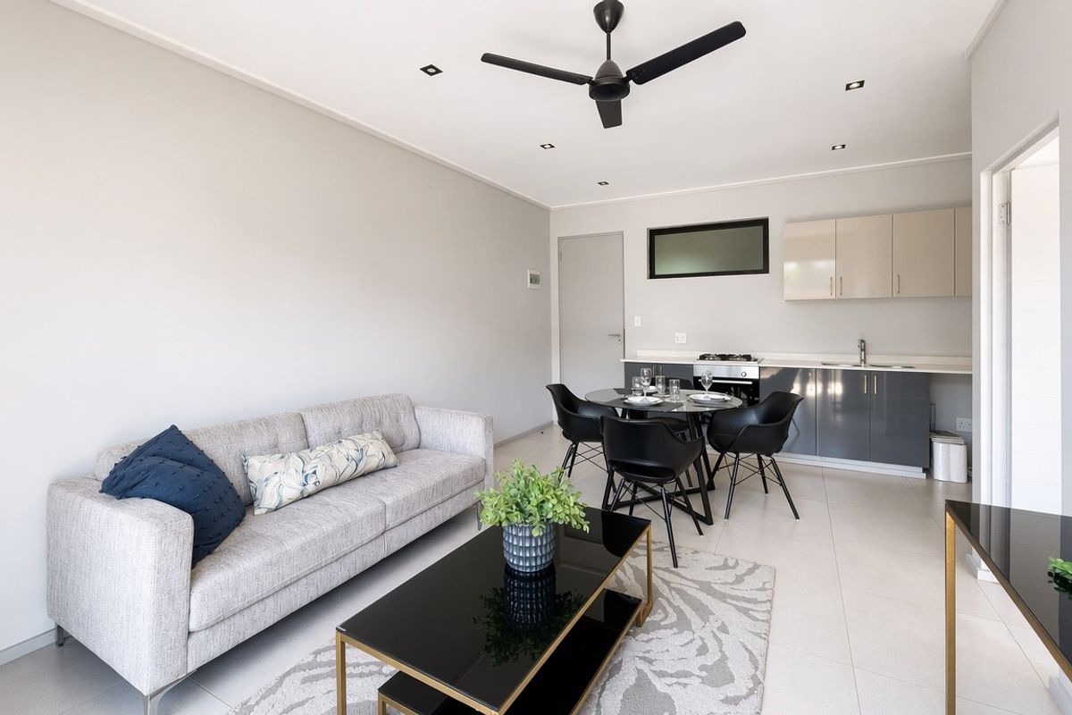 Modern open-plan living area featuring a compact kitchen with built-in cabinetry, sleek tiled flooring, and recessed lighting throughout the space.