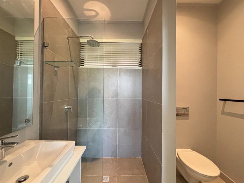 Modern bathroom featuring a walk-in shower with glass screen, wall-mounted toilet, and contemporary vanity basin with neutral tiled finishes.