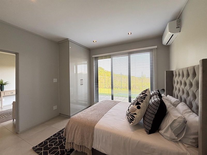 Modern bedroom featuring built-in wardrobes, tiled flooring, recessed lighting, and a wall-mounted air conditioning unit with large windows and venetian blinds.