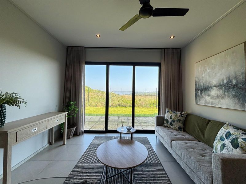A bright living room featuring tiled floors, recessed lighting, a ceiling fan, and large sliding glass doors opening to a rear patio and garden view.