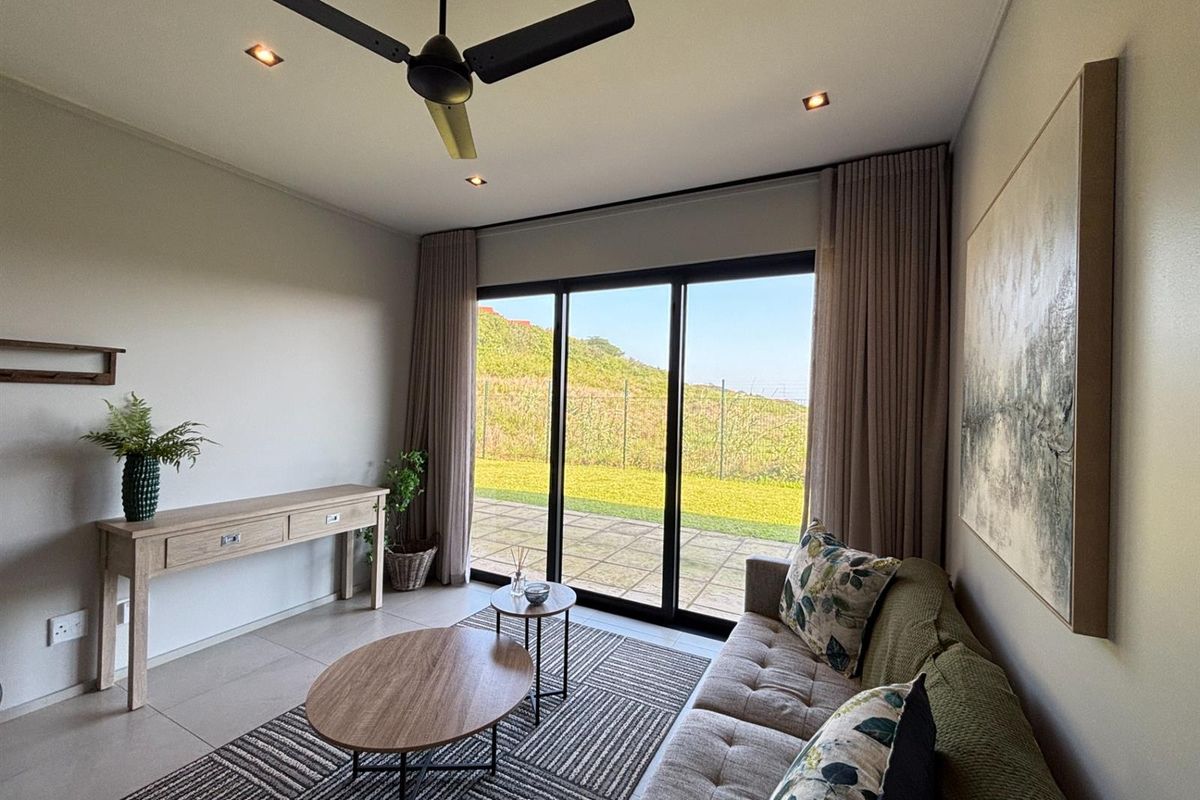 A bright and modern living room featuring tiled floors, recessed lighting, a ceiling fan, and large sliding glass doors leading to an outdoor patio area.