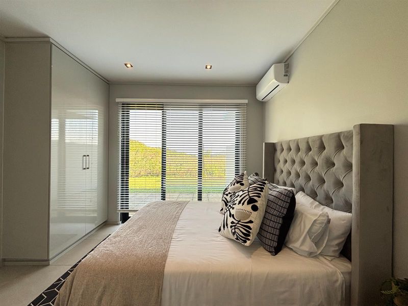 Modern bedroom featuring high-gloss built-in cupboards, recessed lighting, a split-system air conditioner, and large sliding glass doors with venetian blinds.