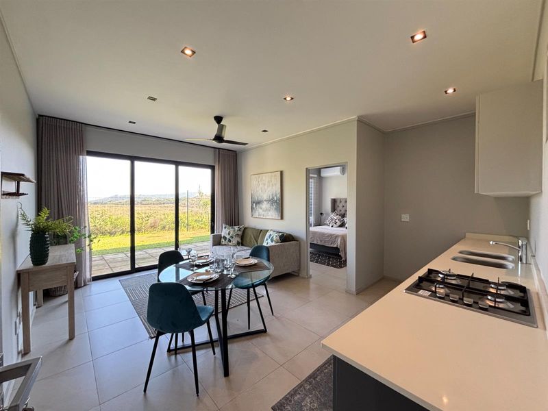 Modern open-plan living area featuring a kitchen with gas hob, tiled floors, recessed lighting, and large sliding doors leading to an outdoor patio.