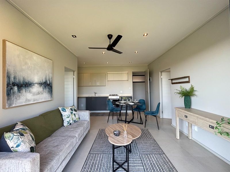 Modern open-plan living area featuring a functional kitchen with built-in cabinetry, oven, and hob, seamlessly flowing into a comfortable dining and lounge space.
