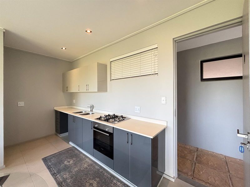 A clean, modern kitchen featuring grey and white cabinetry, a gas hob, built-in oven, and stainless steel sink, with neutral tiled flooring.