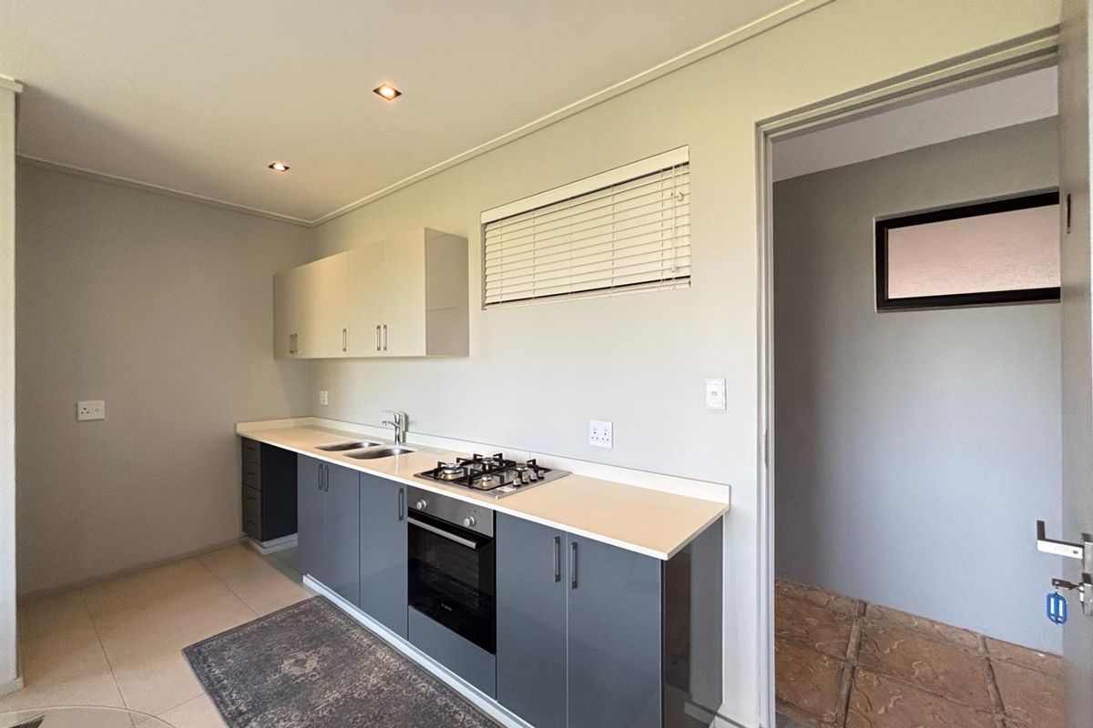 A clean, modern kitchen featuring grey and white cabinetry, a gas hob, built-in oven, and stainless steel sink, with neutral tiled flooring.