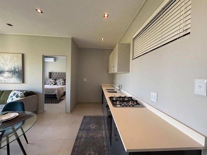 Modern kitchen featuring a gas hob, double sink, and sleek built-in cabinetry, with an open-plan layout leading into the adjacent bedroom.
