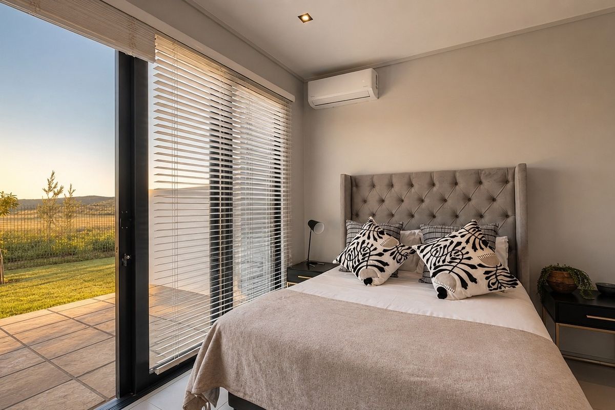 Modern bedroom featuring tiled floors, a split-system air conditioner, and large sliding glass doors opening onto a private patio with garden views.