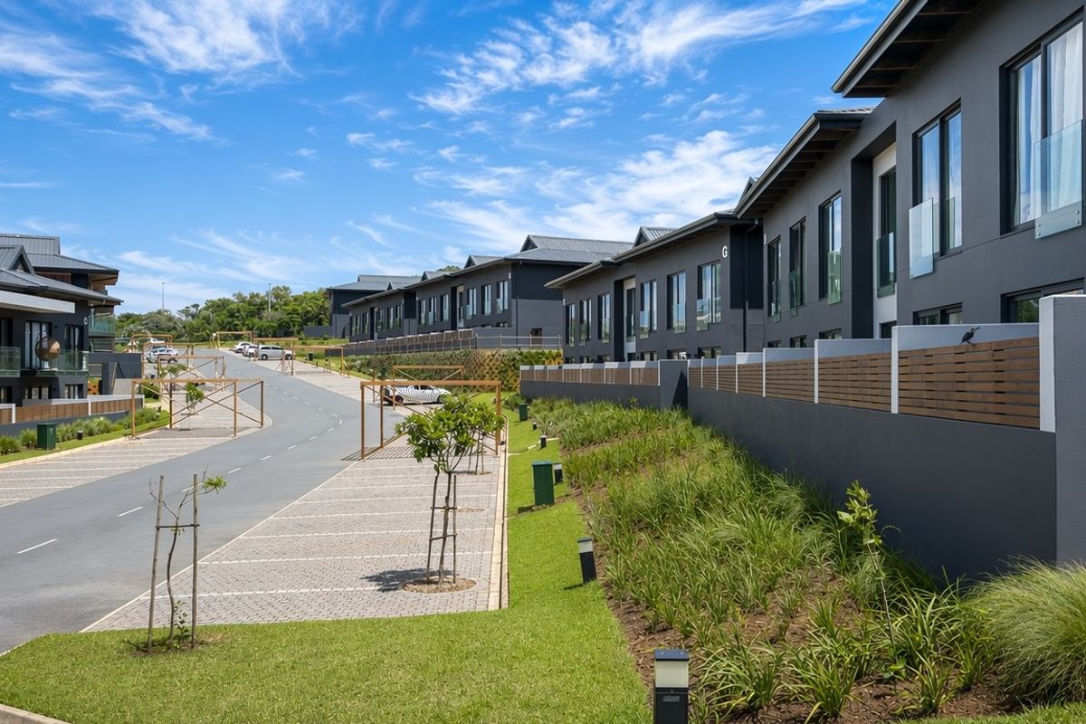 A view of a modern apartment complex streetscape featuring paved parking, landscaped gardens, and contemporary dark-toned building facades.