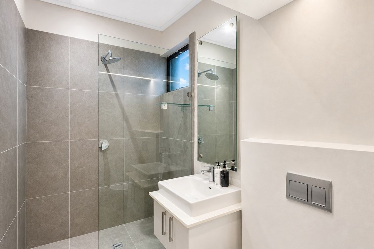 Modern bathroom featuring a walk-in shower with glass screen, wall-mounted vanity with basin, and contemporary tiled finishes.