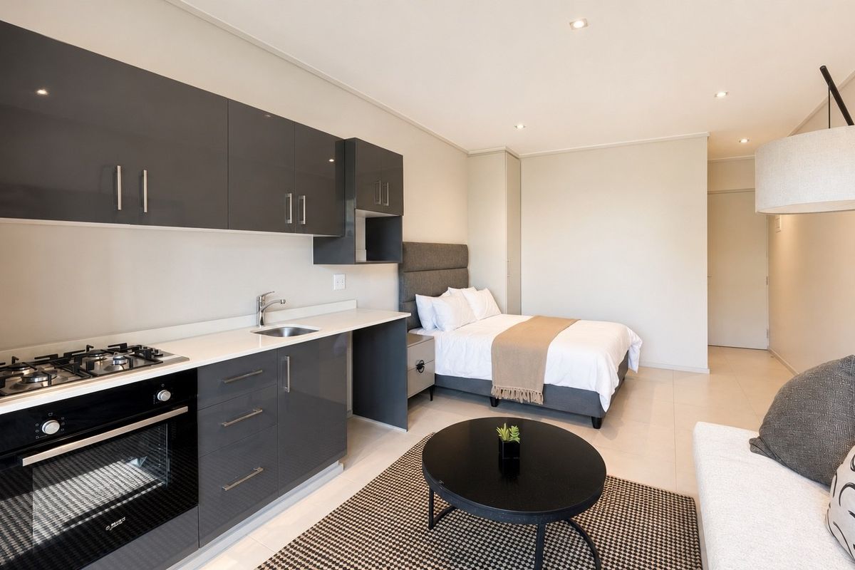 Modern open-plan studio apartment featuring a sleek kitchen with dark grey cabinetry, gas hob, and integrated oven, seamlessly flowing into the bedroom area.