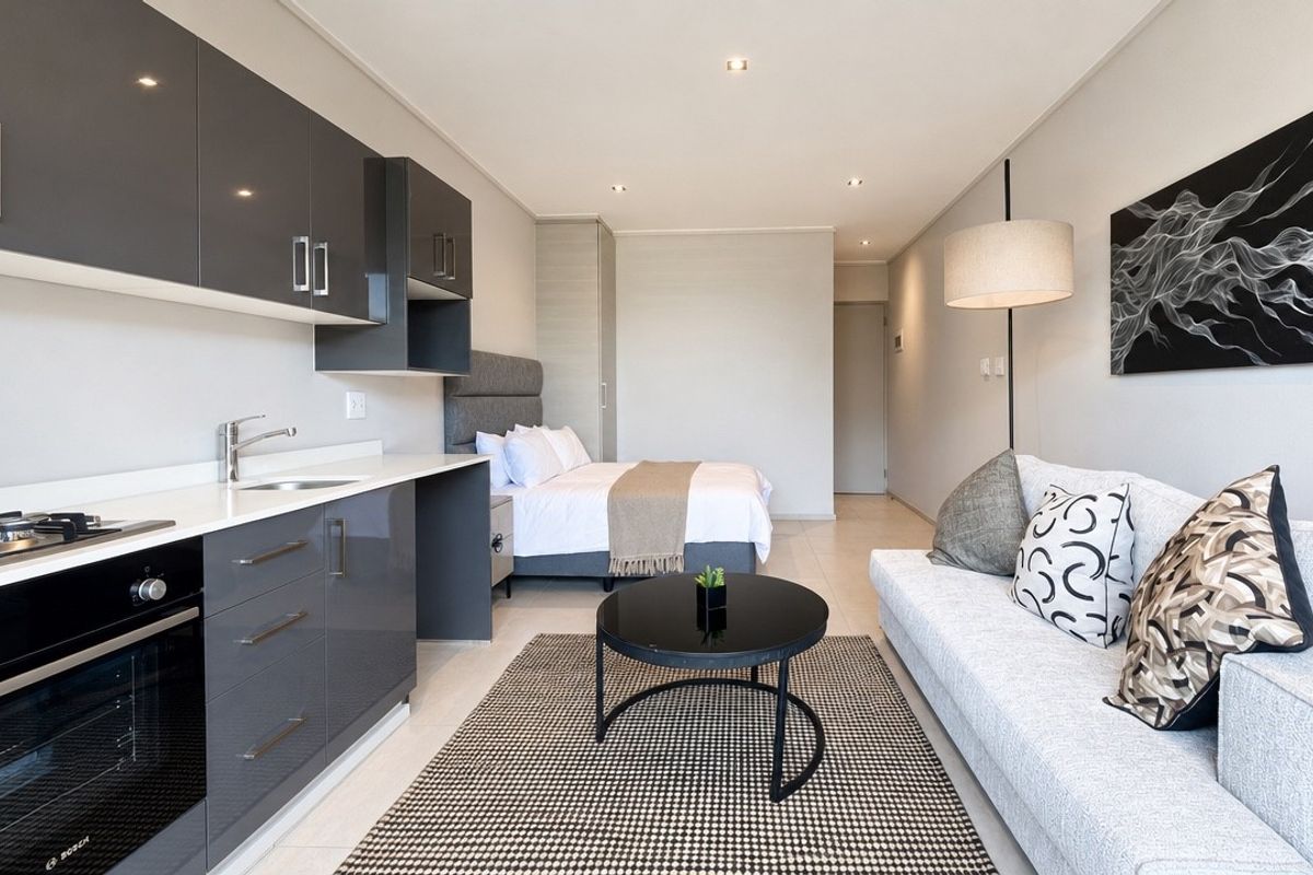 Modern open-plan studio apartment featuring a sleek kitchen with high-gloss cabinetry, integrated appliances, and a seamless transition to the bedroom and living area.