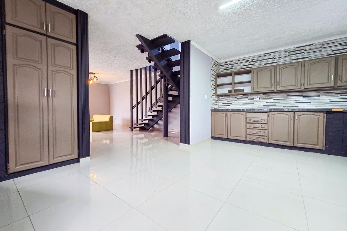 Open plan living area featuring tiled flooring, a central staircase, and built-in kitchen cabinetry with a decorative tiled backsplash.