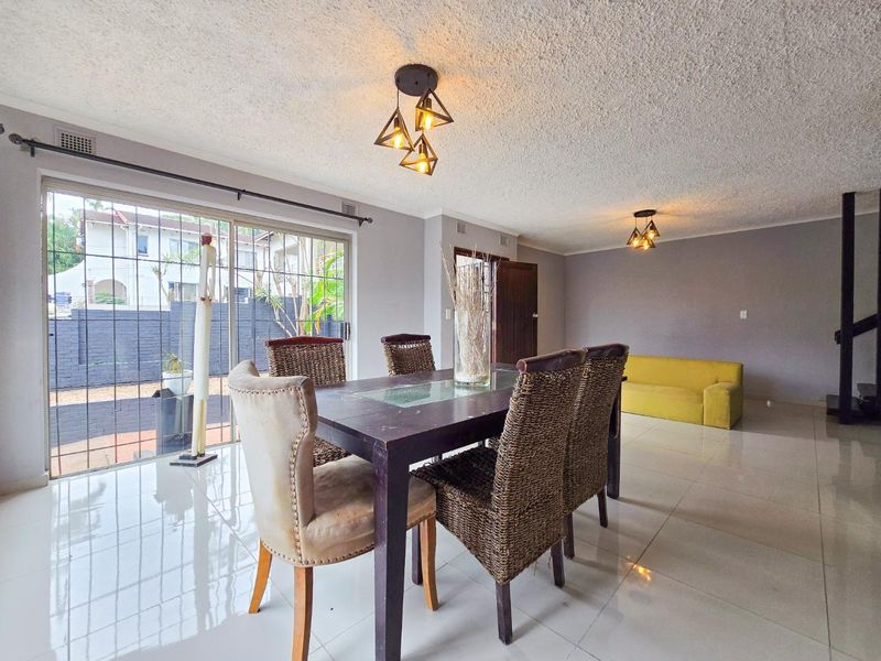 Spacious open-plan living and dining area featuring polished porcelain floor tiles, modern pendant lighting, and large sliding glass doors with security bars.