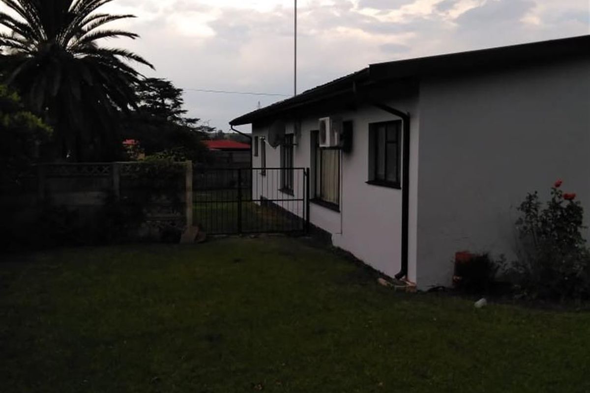 A view of the rear exterior of the house, featuring a lawn, perimeter fencing, and an external air conditioning unit.
