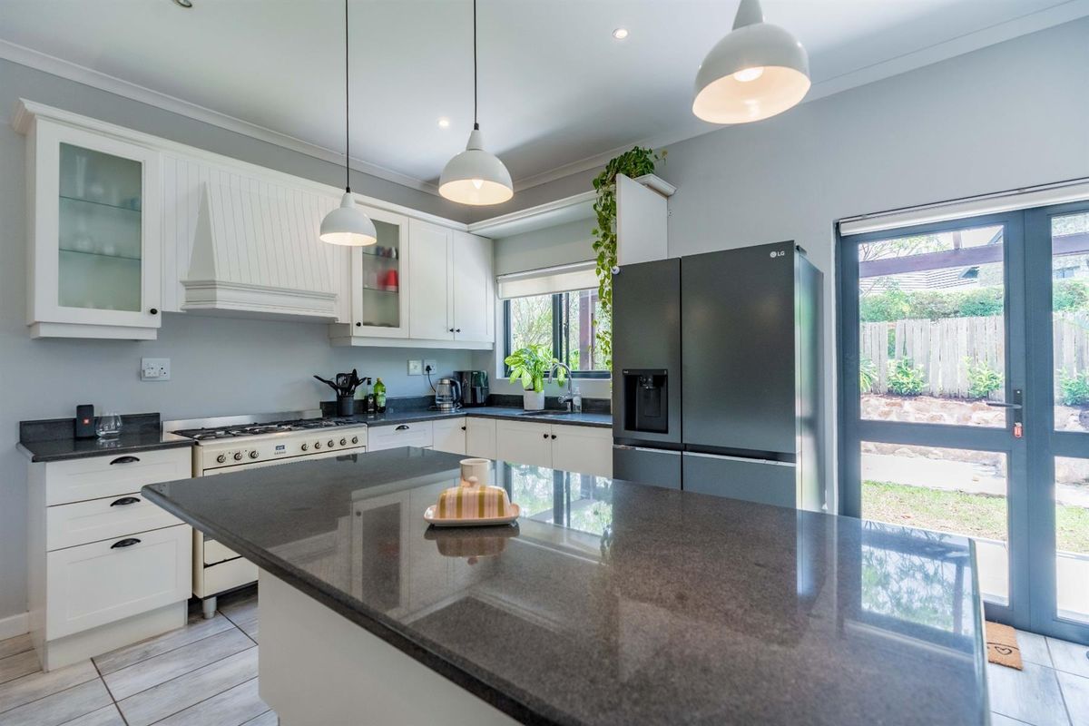 Modern kitchen featuring white cabinetry, dark granite countertops, a central island, and a gas stove, with direct access to the rear garden.