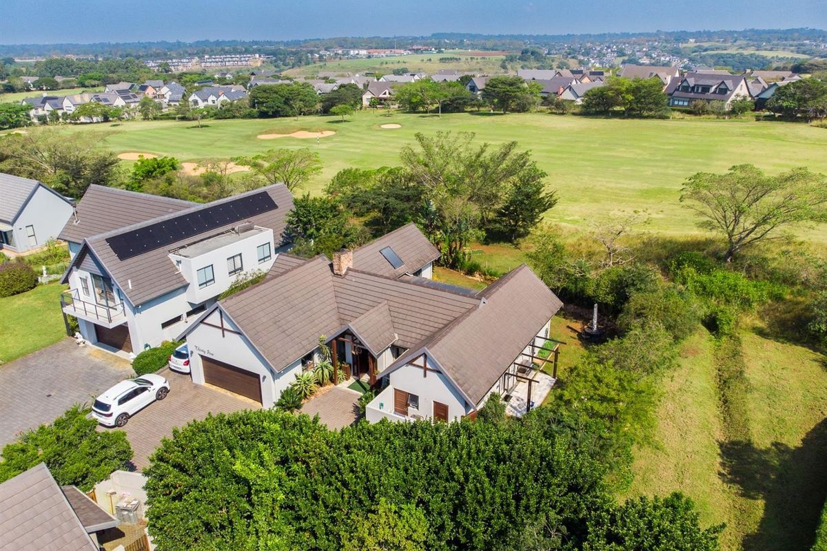 Aerial view of a residential property featuring a tiled roof, solar panels, paved driveway, and a spacious garden overlooking a golf course.