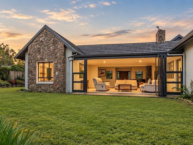 A beautifully maintained rear exterior view featuring stone cladding, a tiled roof, and expansive bi-fold doors opening onto a lush, manicured garden.
