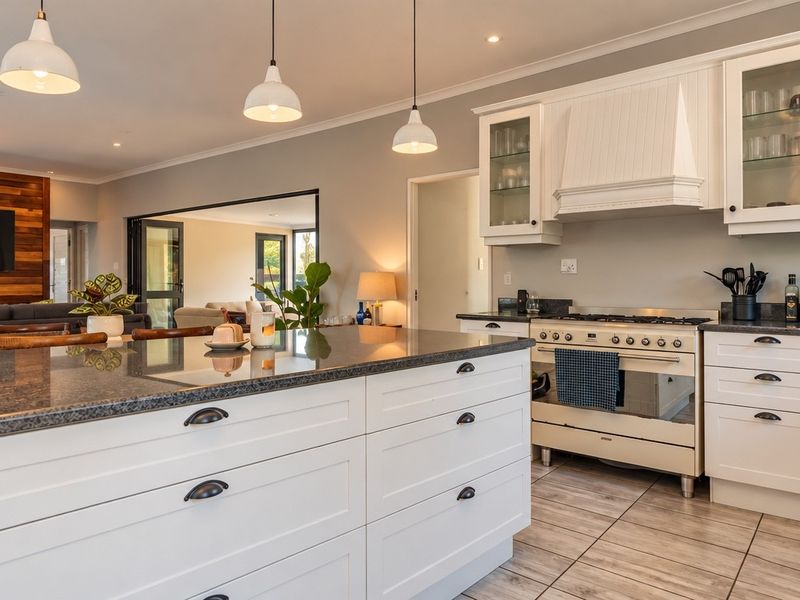 Spacious open-plan kitchen featuring a large island, granite countertops, shaker-style cabinetry, and a freestanding gas stove, flowing into the adjacent living area.