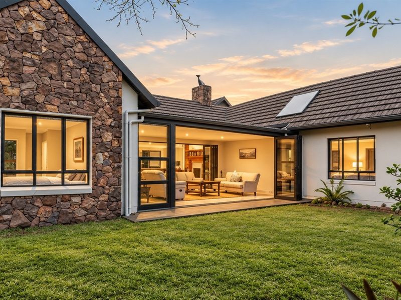 A beautifully maintained rear exterior view featuring stone cladding, a tiled roof with a skylight, and seamless indoor-outdoor flow through large bi-fold doors.