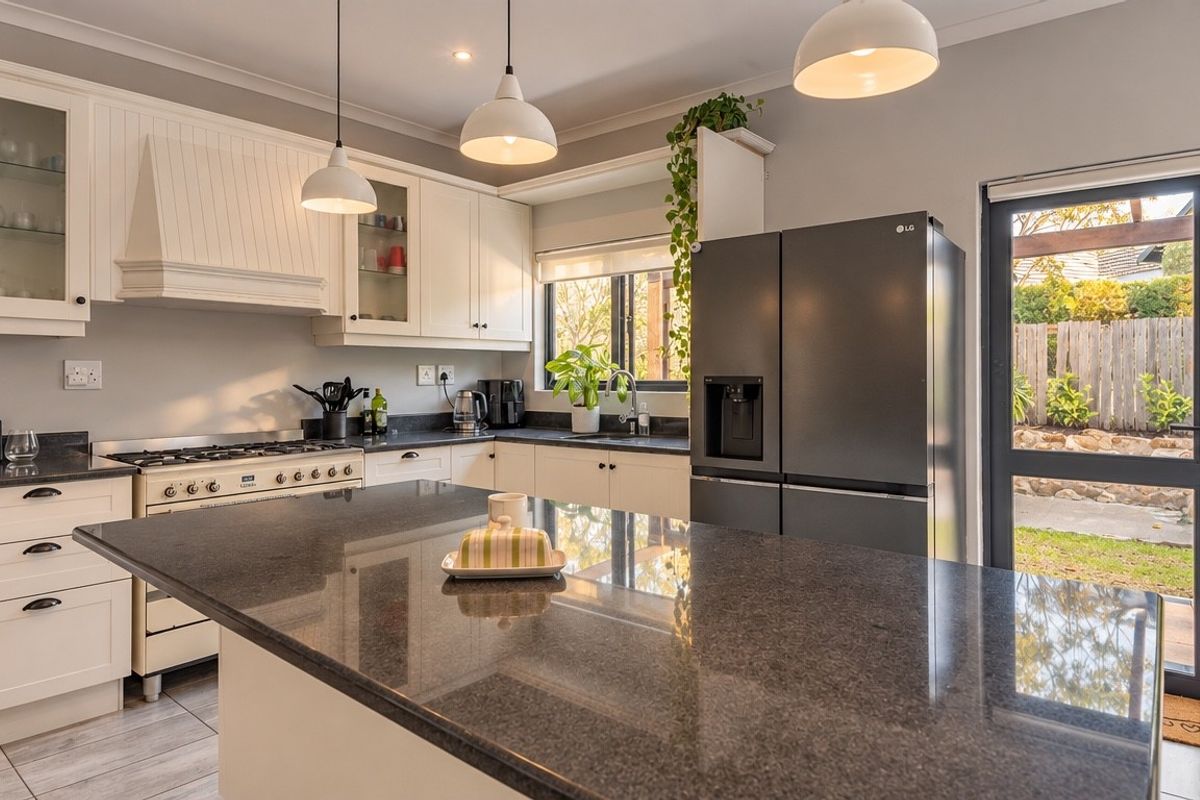Modern kitchen featuring granite countertops, a central island, gas stove, and glass-front cabinetry, with direct access to the rear garden.