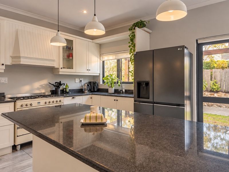 Modern kitchen featuring granite countertops, a central island, gas stove, and glass-front cabinetry, with direct access to the rear garden.