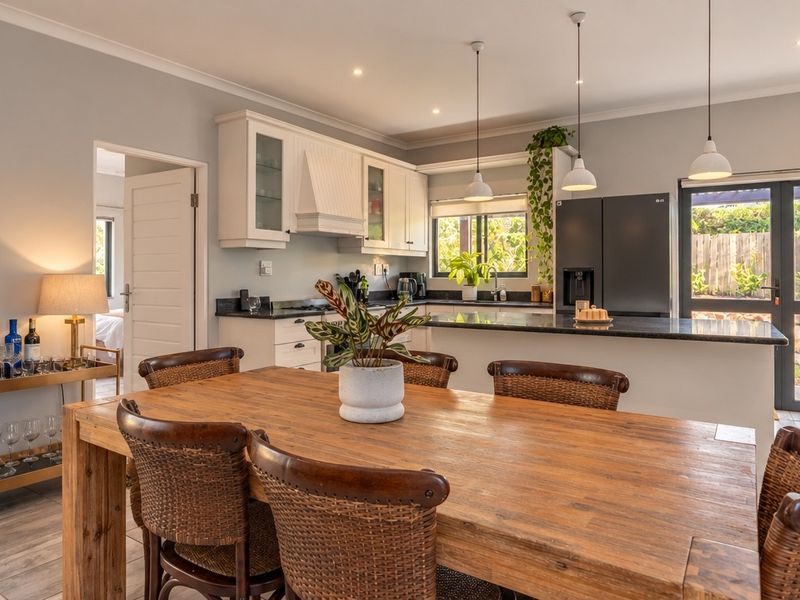 Modern open-plan kitchen and dining area featuring sleek cabinetry, granite countertops, pendant lighting, and direct access to the outdoor patio through glass doors.