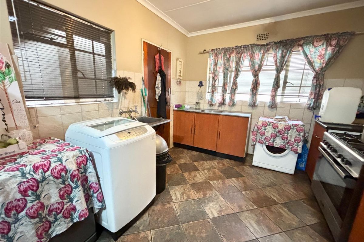 A functional kitchen featuring tiled flooring, built-in wooden cabinetry, a stainless steel sink, and space for laundry appliances.