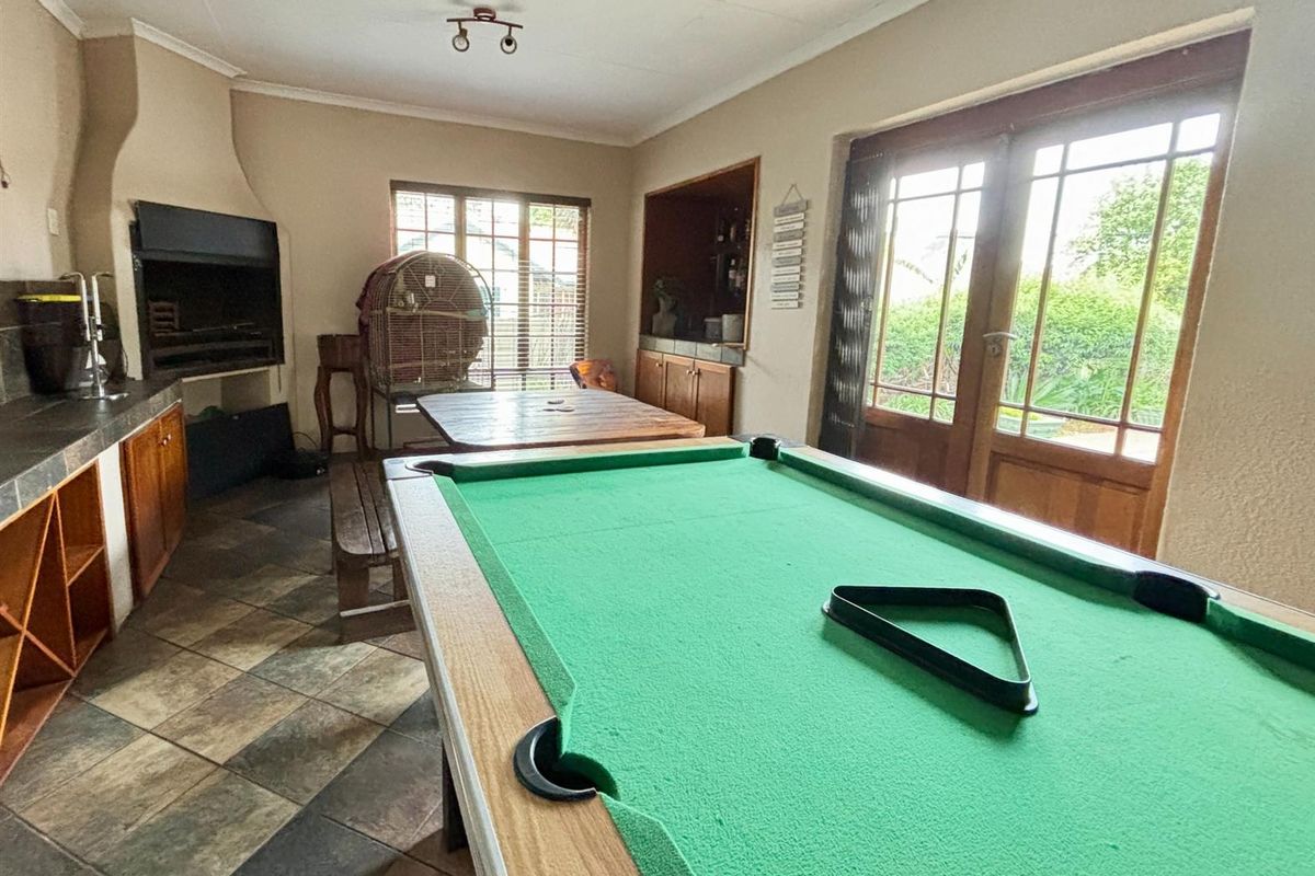 Entertainment room featuring a built-in braai, integrated bar area, tiled flooring, and double doors opening to the garden.