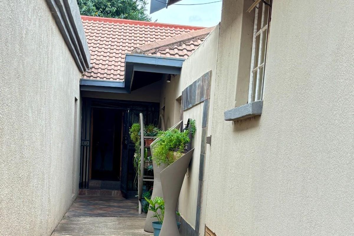 A narrow side walkway leading to the entrance, featuring concrete paving, tiled wall accents, and a security gate at the doorway.