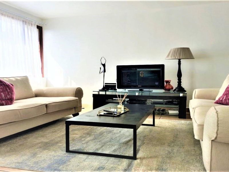 A bright and comfortable living room featuring tiled flooring and a large window that allows for ample natural light.