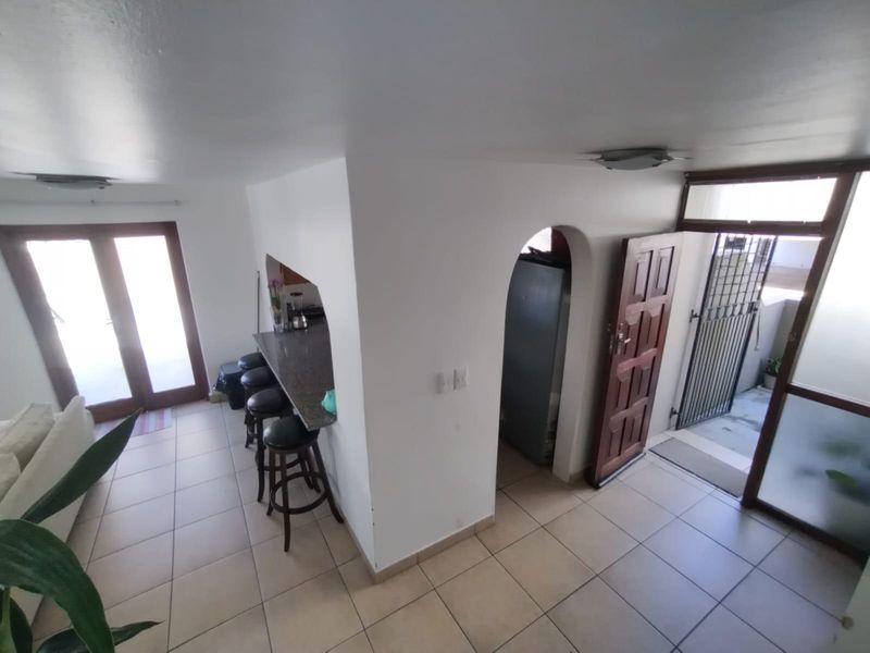 Open plan living area featuring tiled flooring, a granite breakfast bar, and an arched entryway leading to a secondary space with security gate access.