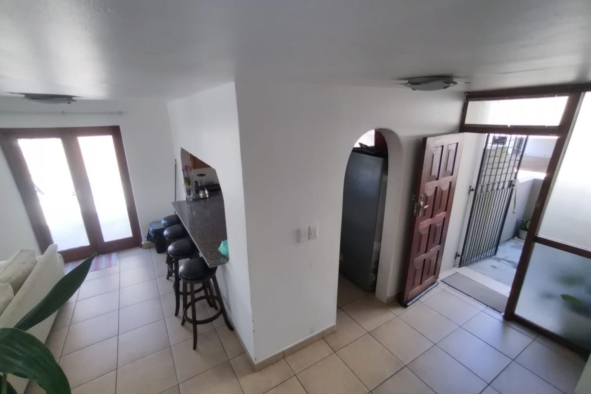 Open plan living area featuring tiled flooring, a granite breakfast bar, and an arched entryway leading to a secondary space with security gate access.