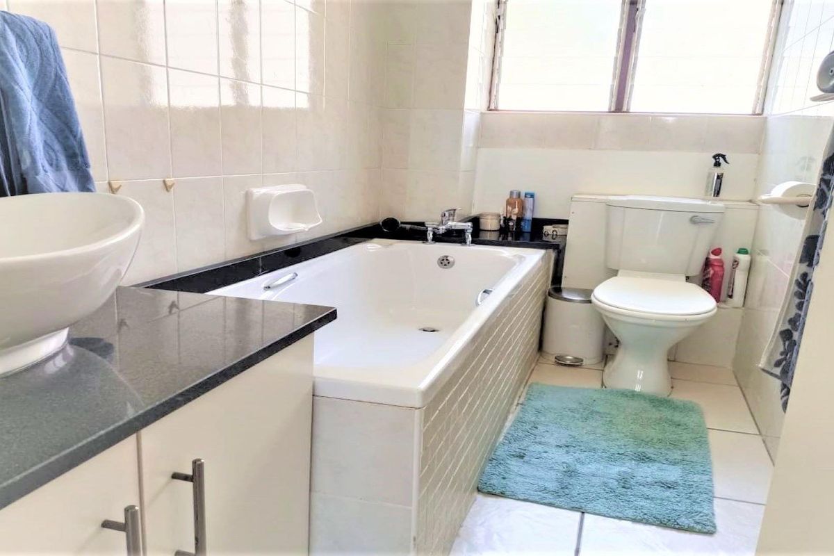 A functional bathroom featuring a built-in bathtub, granite-topped vanity with a vessel sink, tiled walls, and a standard toilet.