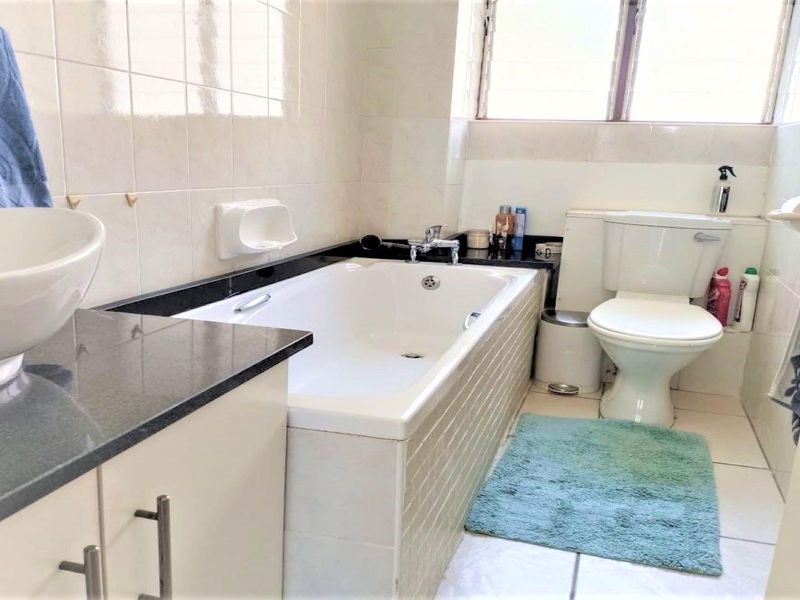 A functional bathroom featuring a built-in bathtub, granite-topped vanity with a vessel sink, tiled walls, and a standard toilet.