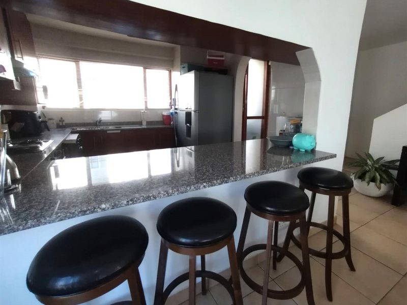 Open plan kitchen featuring a granite breakfast bar, built-in cabinetry, and tiled flooring, seamlessly connecting to the living area.