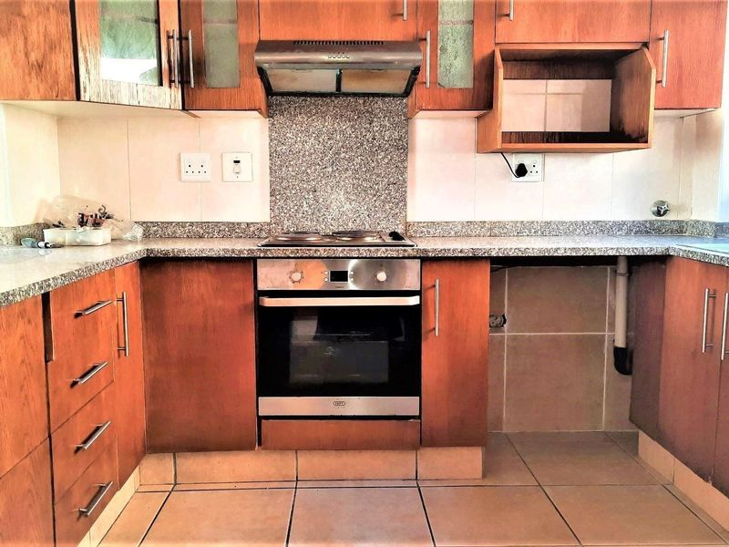A functional kitchen featuring wooden cabinetry, granite countertops, a built-in oven with hob, and a tiled backsplash, offering a practical layout for daily use.