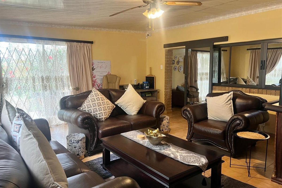 A spacious living room featuring tiled flooring, a ceiling fan, and sliding glass doors with security gates, leading to an adjacent room.