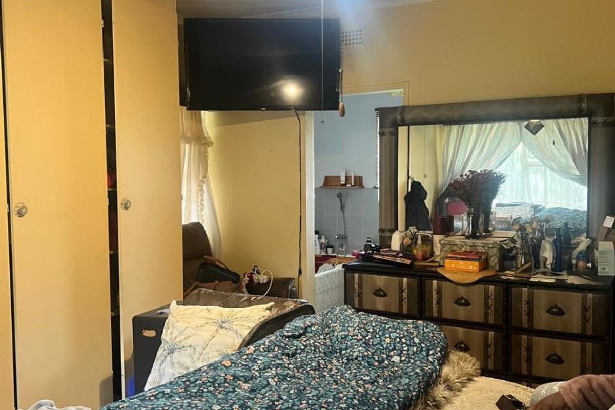 A bedroom featuring built-in cupboards and a ceiling fan, with an adjoining en-suite bathroom visible in the background.