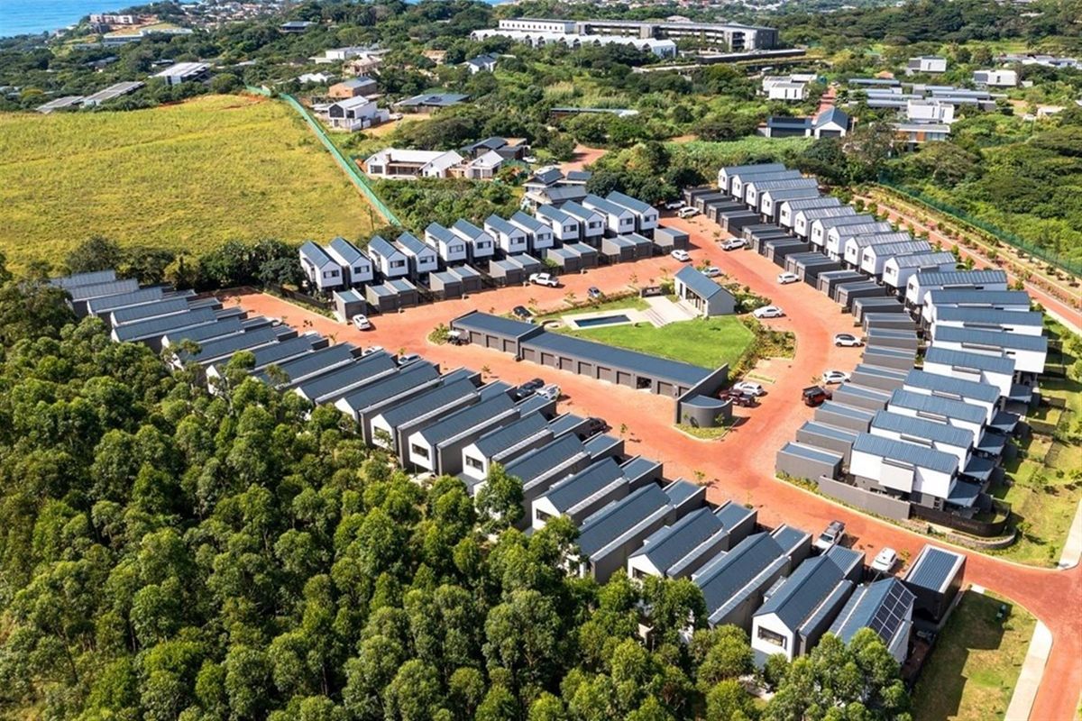 Aerial view of a modern townhouse estate featuring uniform architectural design, paved access roads, communal green spaces, and a central swimming pool area.