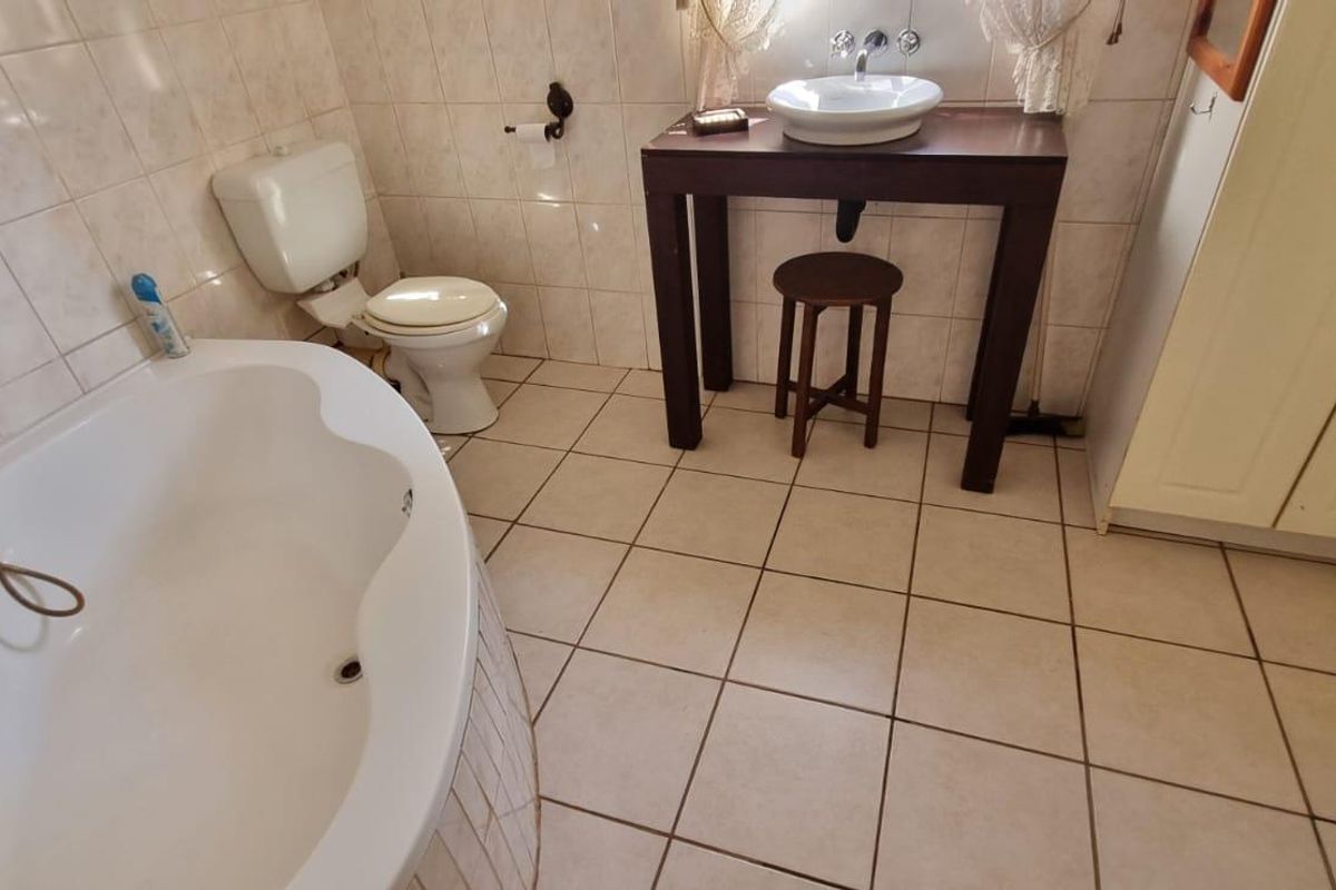 A functional bathroom featuring a corner bathtub, a wall-mounted toilet, and a vessel sink set on a wooden vanity unit with tiled walls and flooring.
