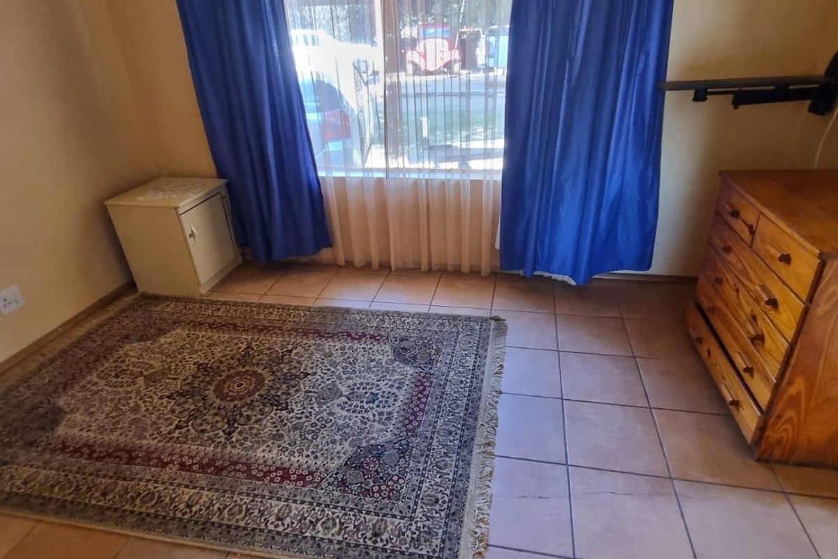 A bedroom featuring tiled flooring, a large window with curtains, and built-in electrical outlets.